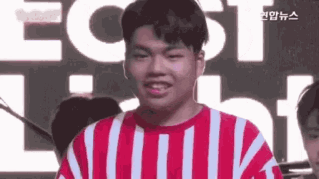 a young man in a red and white striped shirt is smiling in front of a group of people .