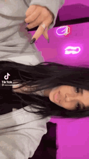a woman with long black hair is standing in front of a purple wall and a neon sign that says tik tok