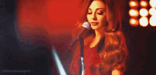a woman is singing into a microphone on a stage in front of a red background .