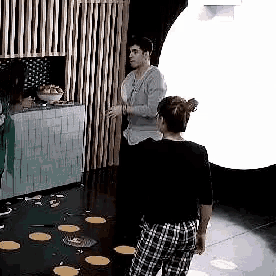 a man and a woman are standing next to each other in a room . the woman is wearing plaid pants .