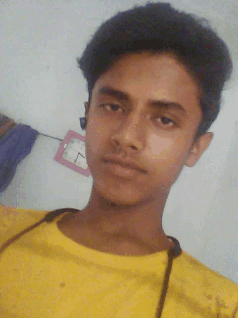 a young man in a yellow shirt looks at the camera with a clock in the background