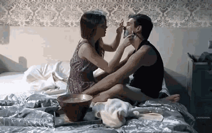 a man and a woman are sitting on a bed applying makeup to each other .