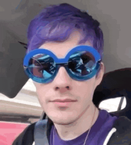 a man with purple hair is wearing sunglasses and a purple shirt .