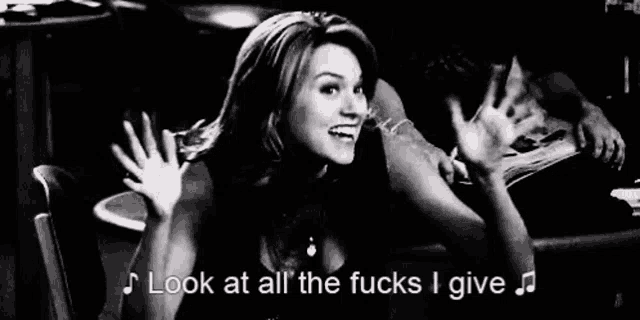 a woman is sitting in a chair with her hands in the air and says `` look at all the fucks i give `` .