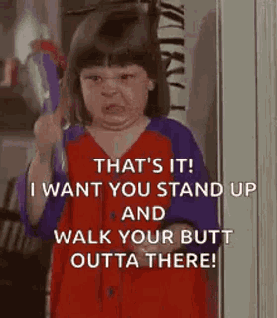 a little girl is standing in front of a door holding a brush and making a face .