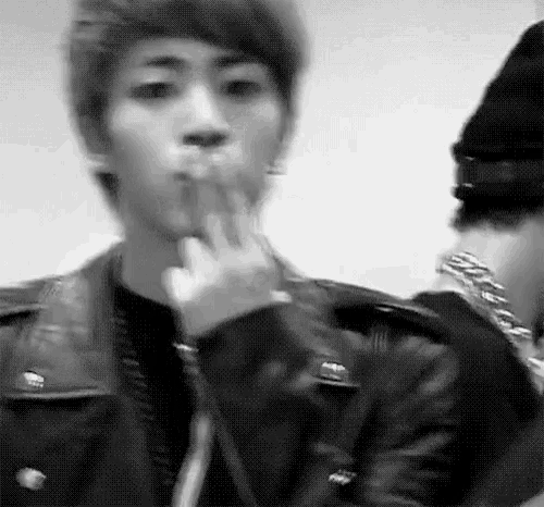 a black and white photo of a young man in a leather jacket smoking a cigarette .