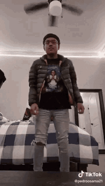 a man is standing in front of a bed wearing a jacket and jeans .