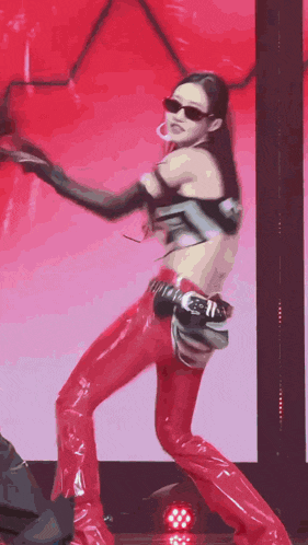 a woman is dancing on a stage wearing red pants and sunglasses .