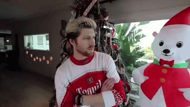 a man wearing an ugly christmas sweater stands next to a tequil polar bear