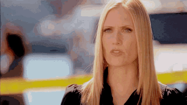 a woman with long blonde hair and a black shirt is making a serious face