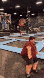 a man in a red shirt is jumping on a trampoline in a gym
