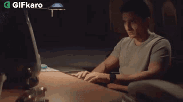 a man is sitting at a desk talking on a phone with a gifkaro logo in the background