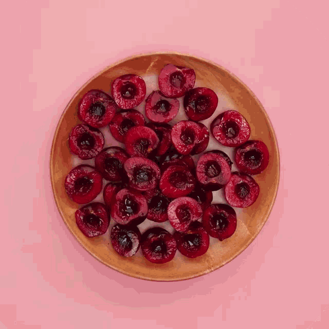 a wooden bowl filled with cherries on a pink surface