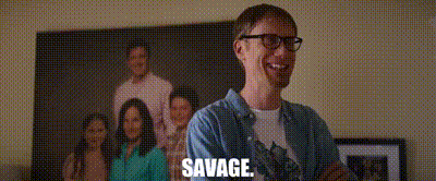 a man wearing glasses is standing in front of a picture of a family and says savage .