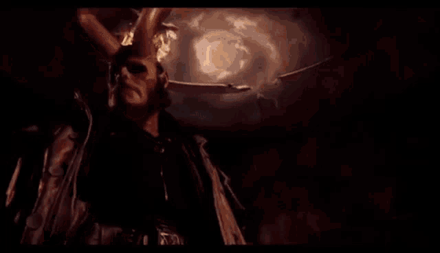 a demon with horns is standing in a dark room with a sword in his hand .