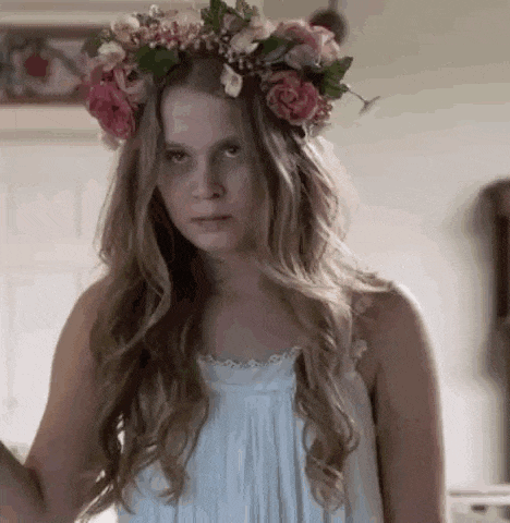 a woman wearing a flower crown and a white dress is making a funny face .
