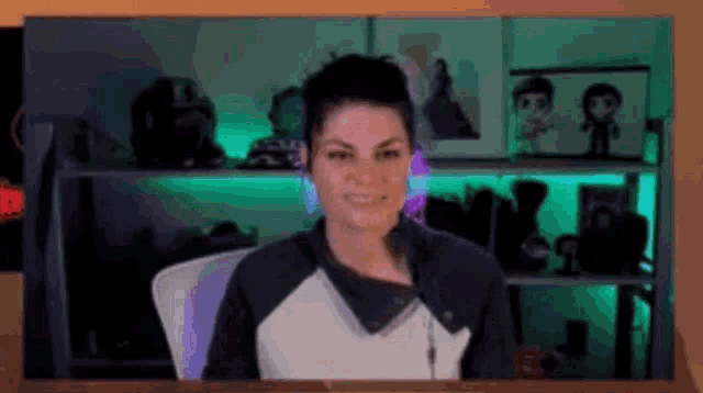 a woman is sitting at a desk in front of a shelf with green lights behind her .