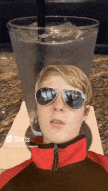 a man wearing sunglasses and a red jacket is sitting in front of a large glass of water