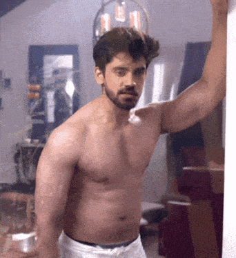 a shirtless man leans against a wall with his arm up