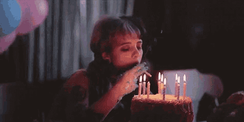 a woman is blowing out candles on a birthday cake while smoking a cigarette .