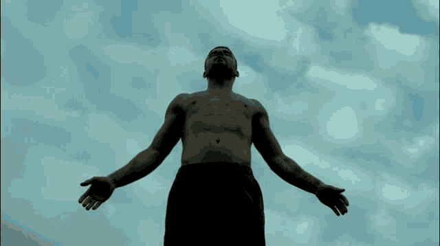 a man without a shirt is standing with his arms outstretched in front of a cloudy sky