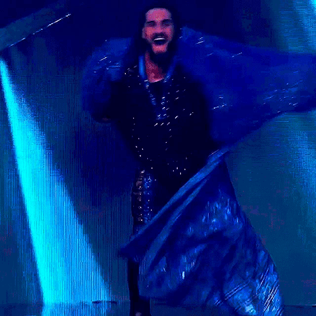 a man in a long blue cape is dancing on stage