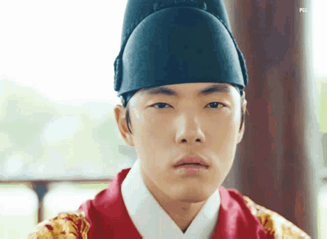 a young man wearing a black hat and a red and gold kimono .