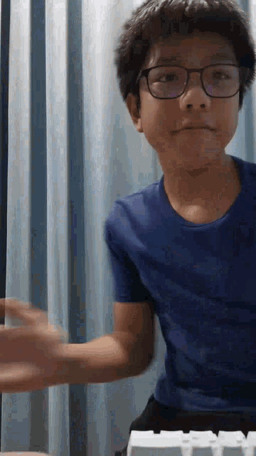 a young boy wearing glasses and a blue shirt playing a keyboard