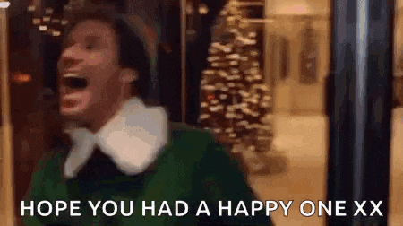 a man in a green sweater is laughing with his mouth open in front of a christmas tree in a store .