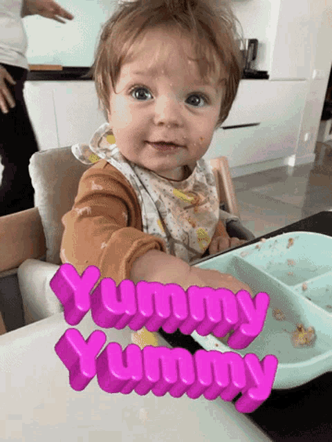 a baby is sitting in a high chair with the words yummy yummy on the table
