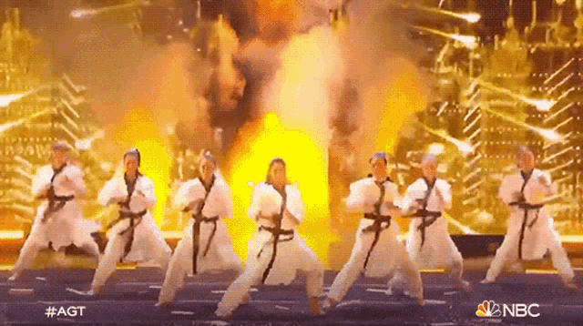 a group of karate fighters are performing on a stage with a fire explosion in the background .
