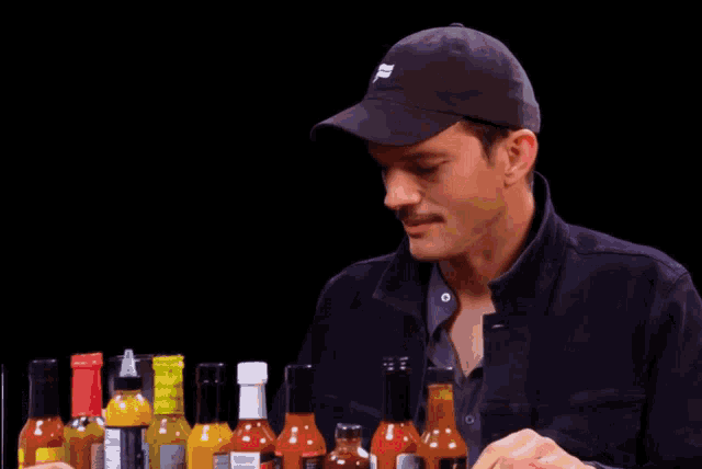 a man wearing a hat that says ' abercrombie & fitch ' on it looks at bottles of hot sauce
