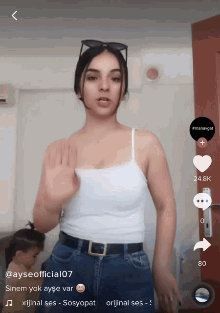 a woman in a white tank top and blue jeans is on a social media platform