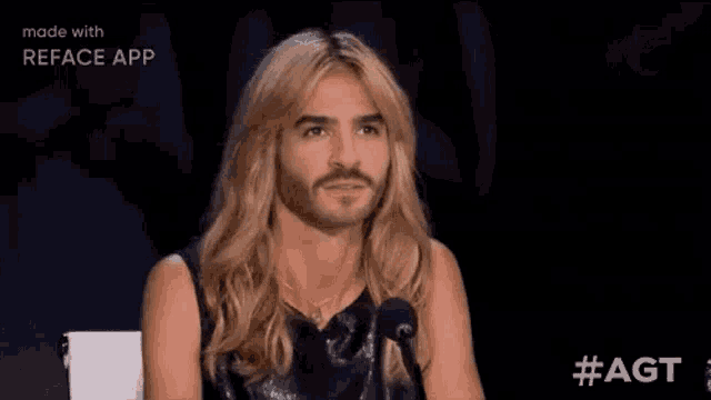 a man with long blonde hair and a beard is sitting in front of a microphone on a stage .