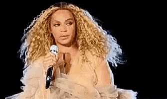 a woman with curly hair is holding a microphone in her hand .