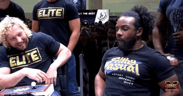 a man wearing a shirt that says elite sits next to another man wearing a shirt that says silly casual