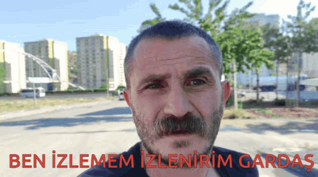 a man with a mustache is standing in front of a sign that says ben izlemem izlenirim garda