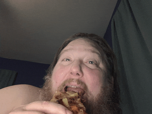 a shirtless man with a beard is eating a pizza