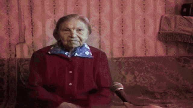 an elderly woman sitting on a couch holding a microphone
