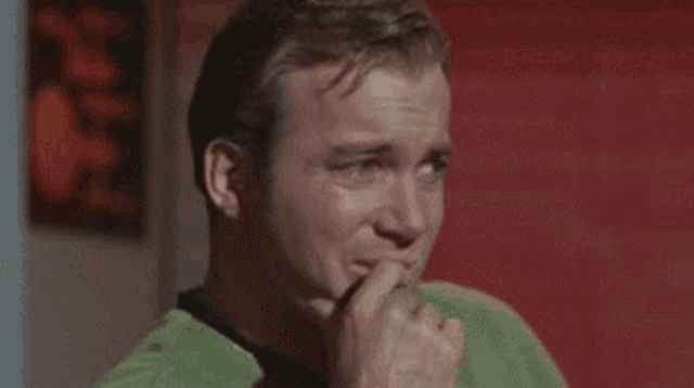 a man in a green shirt is holding his hand to his chin and thinking .