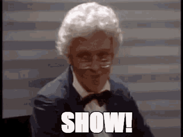 a man with white hair and glasses is wearing a suit and bow tie and says `` show ! ''