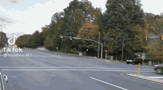 a car is driving down a street with trees in the background and a tiktok logo in the corner .