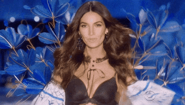 a woman in a black bra is standing in front of a blue background with flowers .
