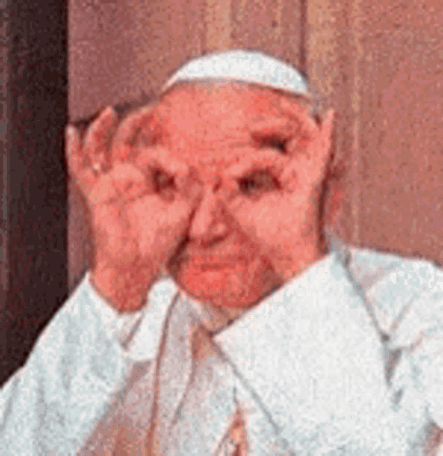 a man is covering his eyes with his hands while wearing a white hat .