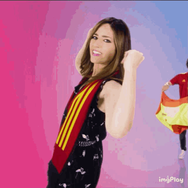 a woman in a black dress with a red and yellow scarf around her neck has a fist in the air