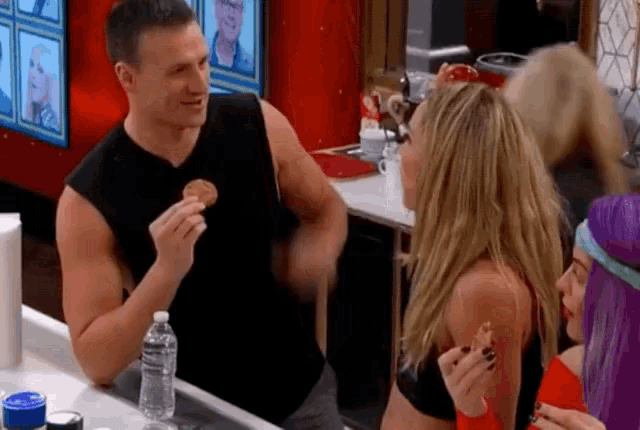 a man in a black tank top holds a piece of food in his hand