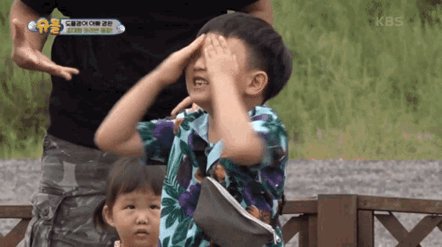 a little boy covering his face with his hands while a little girl looks on