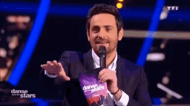 a man in a suit is holding a microphone and holding a dance stars magazine .