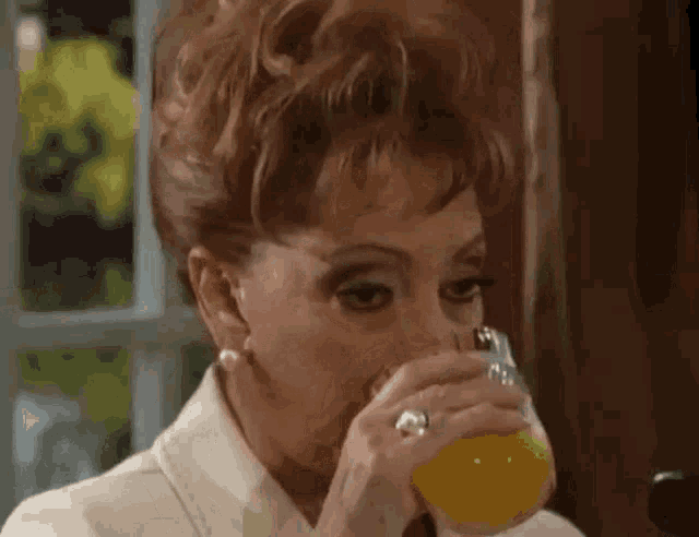 a woman drinking orange juice from a glass with a ring on her finger