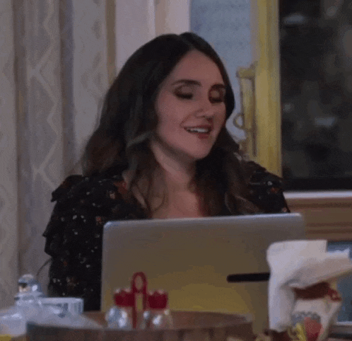 a woman is smiling while sitting at a table with a laptop computer .